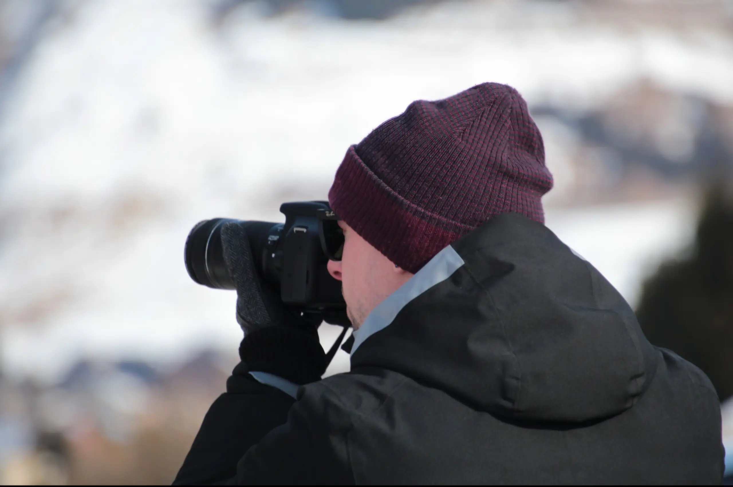 Outdoor winter landscape photography with photographer in knit beanie and technical jacket using a telephoto lens